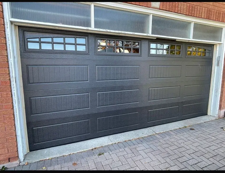 Black carriage-style garage door with upper glass windows installed on a brick home