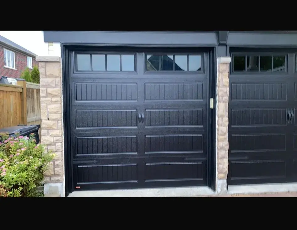 Two black carriage garage doors with upper windows separated by stone columns