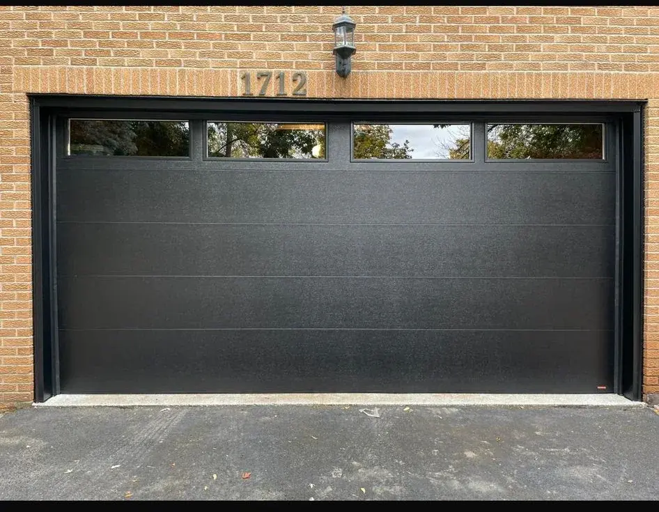 Black flush garage door with narrow top windows installed in a brick opening