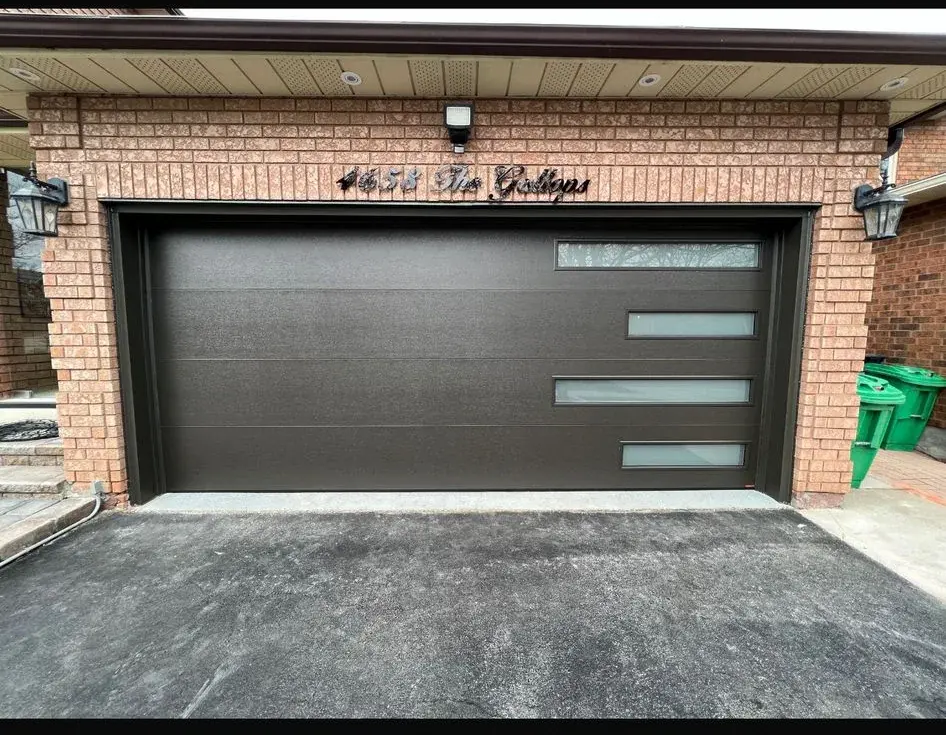 Black modern garage door with stacked side glass panels installed on a brick home