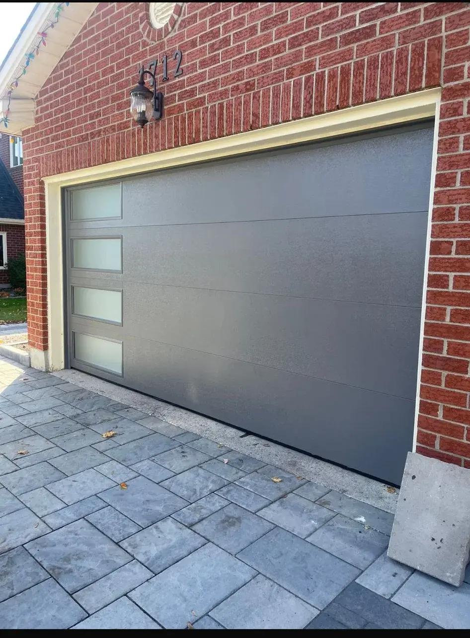 Gray flush modern garage door with vertical glass windows installed on a brick home