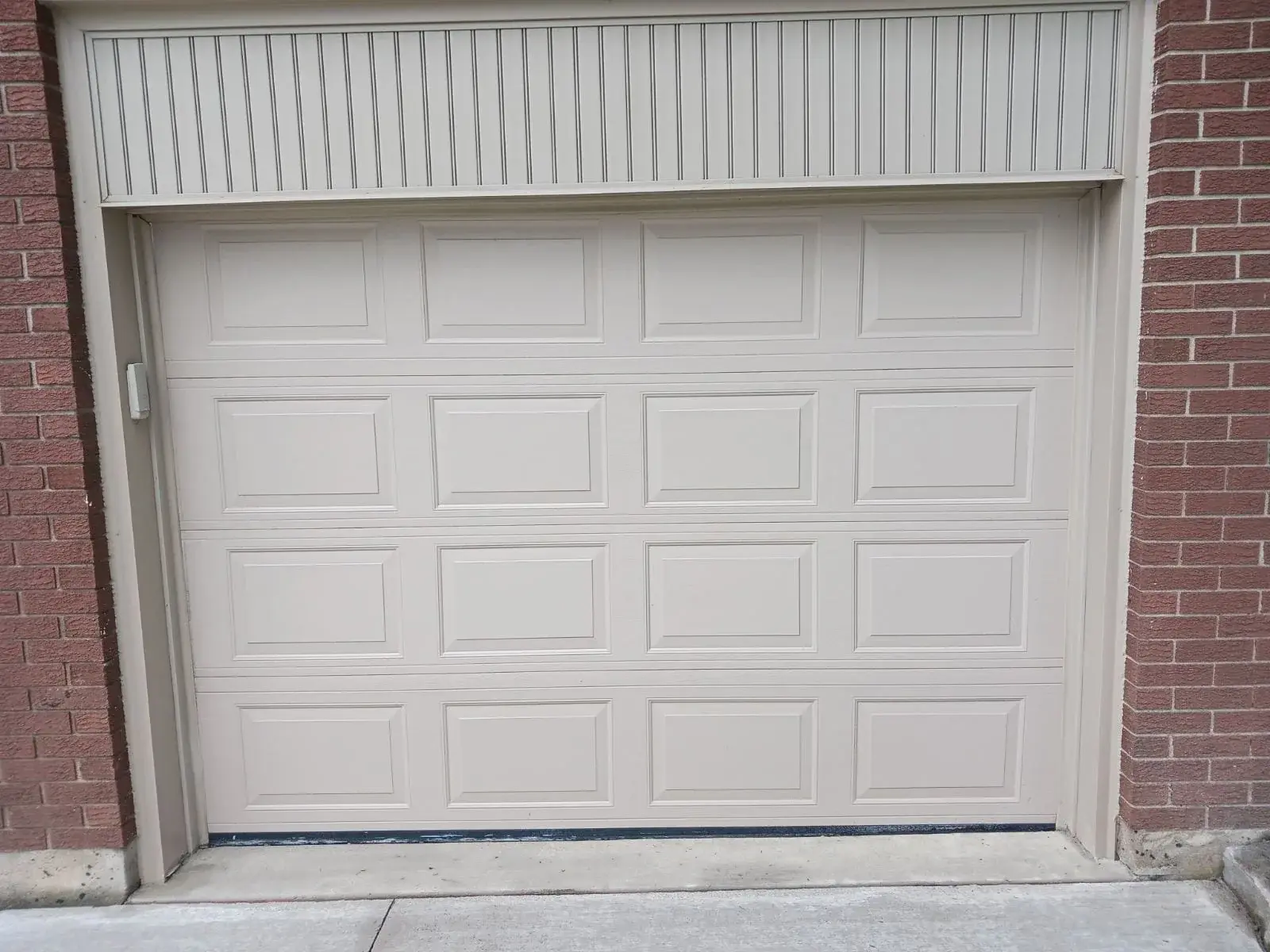 White raised-panel garage door installed between brick columns