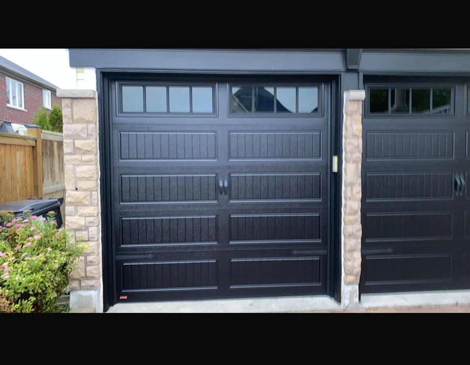 Two black carriage garage doors with upper windows separated by stone columns
