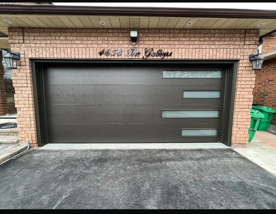 Black modern garage door with stacked side glass panels installed on a brick home