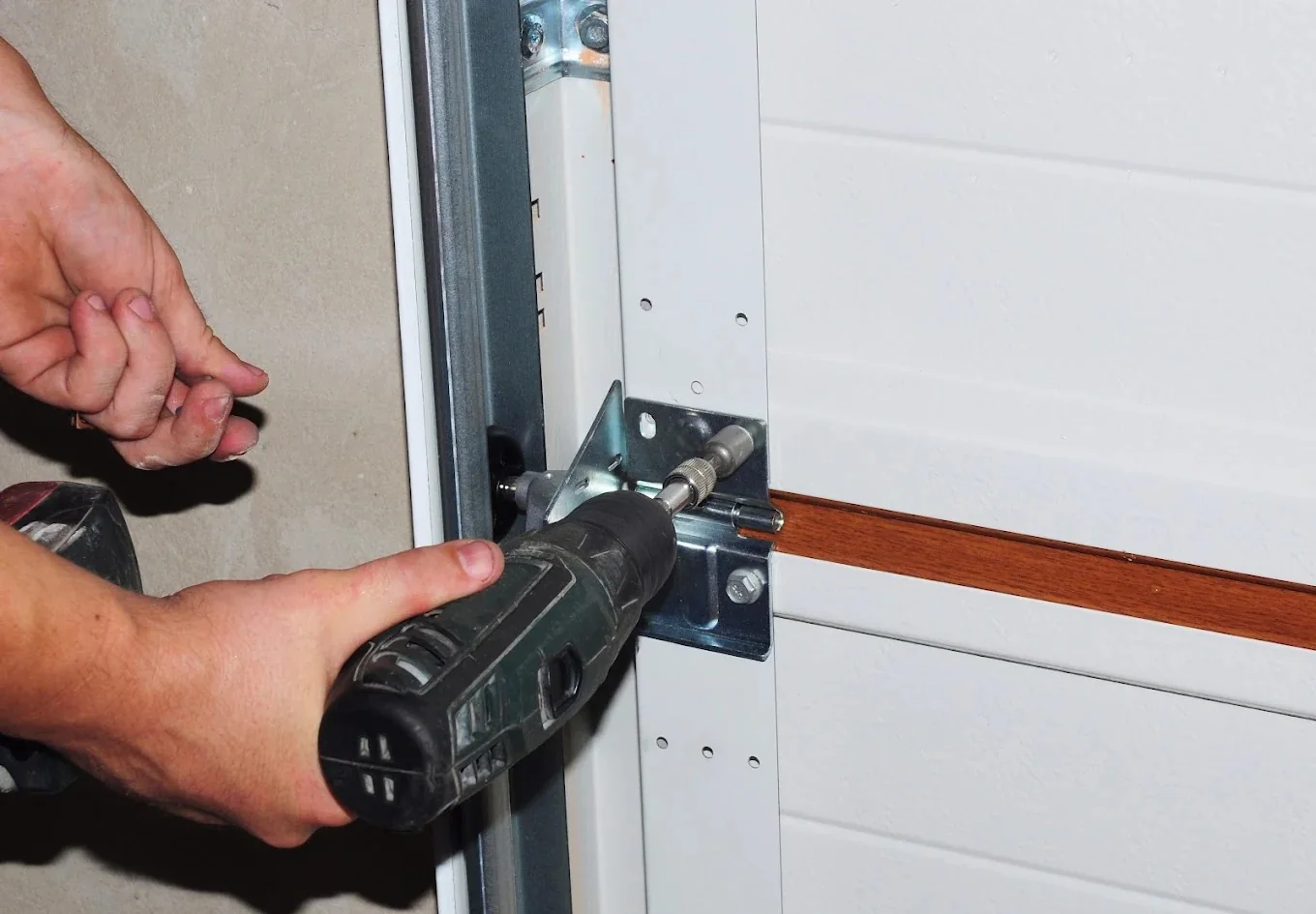 Technician fastening garage door bracket hardware with a drill