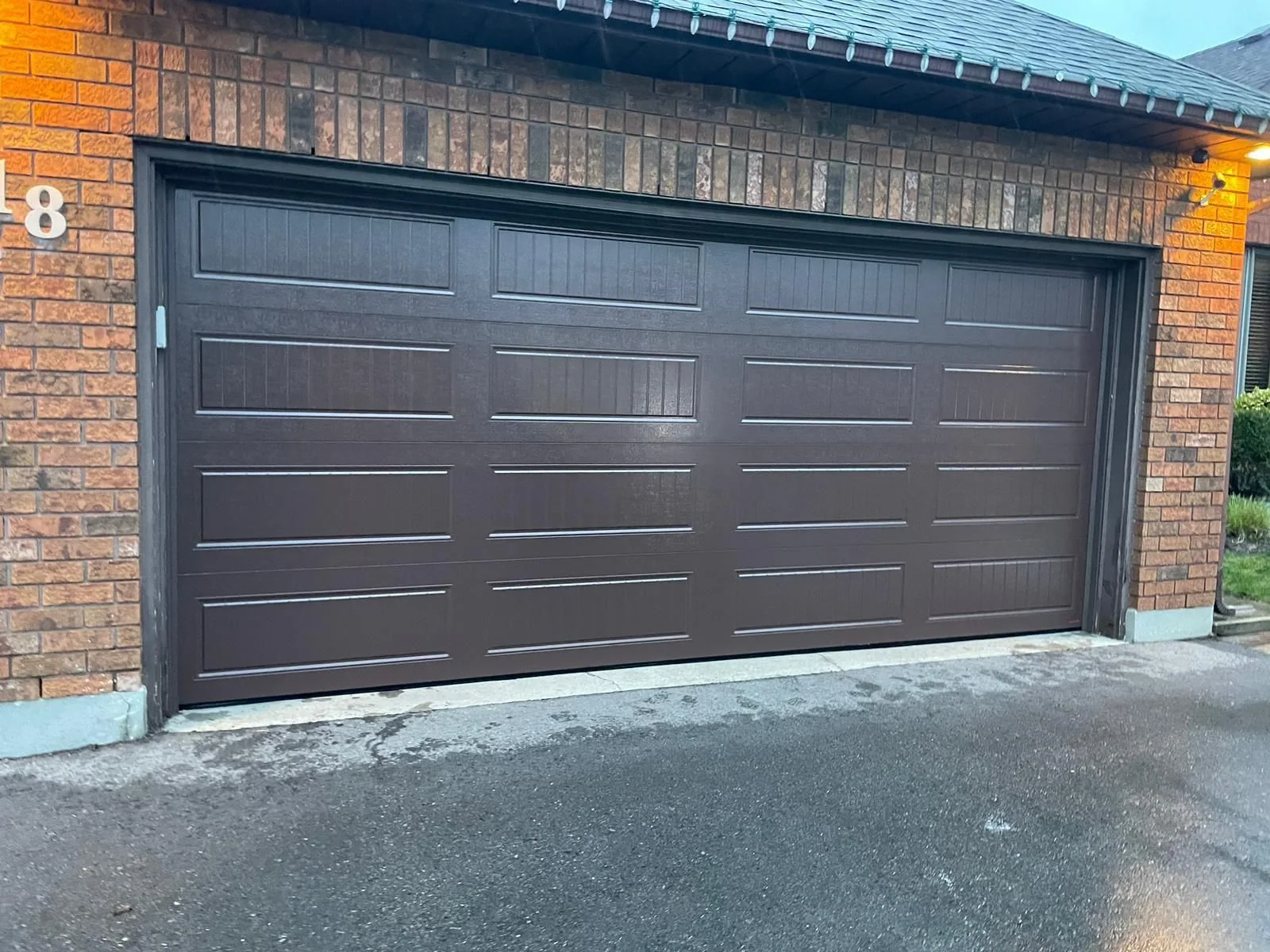 Brown raised-panel garage door installed on a brick home