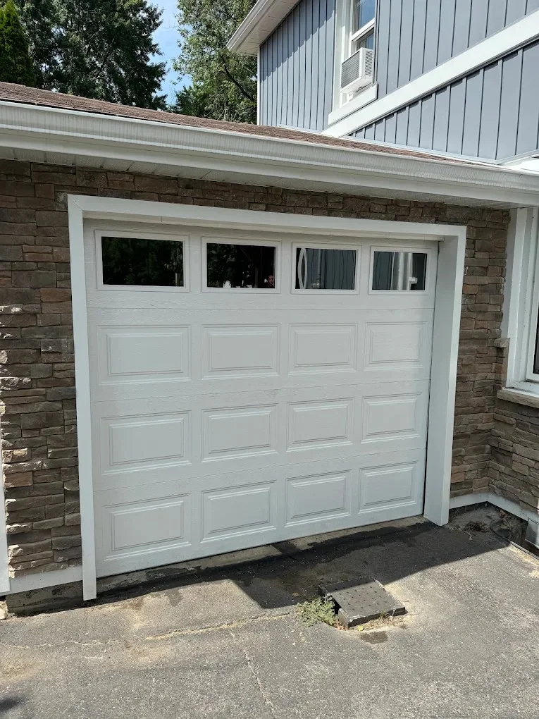 White carriage-style garage door with upper windows installed in a stone opening