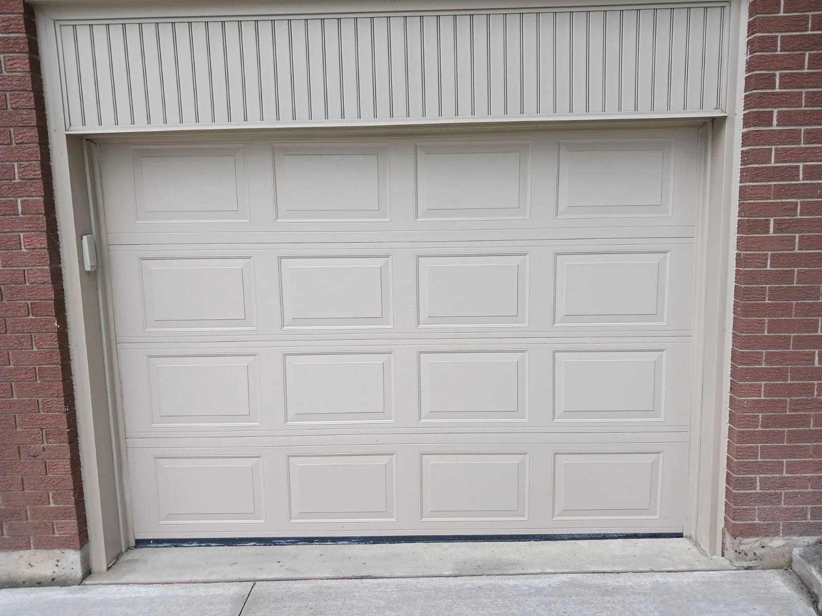 White raised-panel garage door installed between brick columns